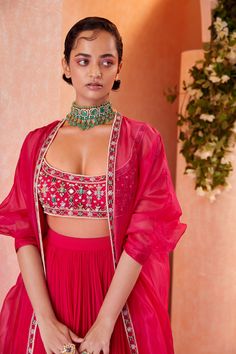 Editor's Note This set features a fuschia net blouse with jeweled embroidery paired with a chiffon ruched skirt and completed with an organza kimono cape. Fabric: Blouse: net, skirt: chiffon, cape: organza Color: Fuschia Components: Skirt, blouse and cape Occasion: Sangeet and Wedding Guest Disclaimer: Product color may slightly vary due to photographic lighting sources or your monitor setting. Care: Dry clean only About the Designer Ridhi Mehra follows a minimalist yet effective design philosop Silk Set With Cape Sleeves For Party, Silk Sets With Cape Sleeves For Party, Silk Party Set With Cape Sleeves, Glamorous Silk Designer Wear Sets, Organza Party Sets With Cape Sleeves, Glamorous Silk Sets For Designer Wear, Silk Lehenga With Cape Sleeves For Party, Party Silk Lehenga With Cape Sleeves, Party Sets With Sheer Dupatta And Cape Sleeves