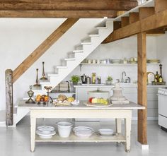 a kitchen with white walls and wooden beams on the ceiling is filled with dishes, cups, bowls, and utensils