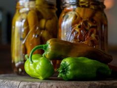 green peppers sitting on top of a wooden table next to jars filled with pickles