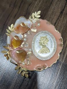 a pink and gold brooch with an image of a woman on the back of it