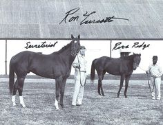 two men standing next to horses in front of a building