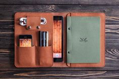 an open leather case with various items in it on a wooden table next to a cell phone