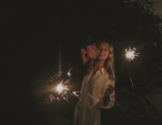 a man and woman standing next to each other holding sparklers