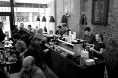 black and white photograph of people eating at tables in a restaurant with brick walls on the wall