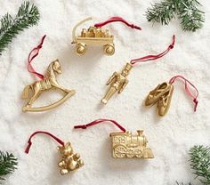 christmas ornaments are laid out on a white surface with pine branches and red ribbon around them