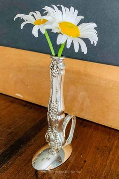 two daisies in a silver vase on a wooden table