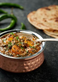 a small metal bowl filled with food next to some pita bread