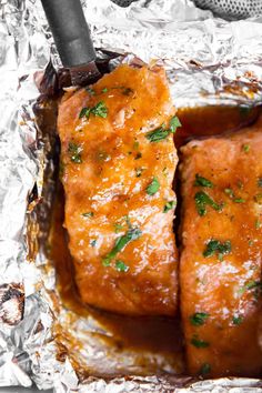 two pieces of meat covered in sauce and garnished with parsley on aluminum foil