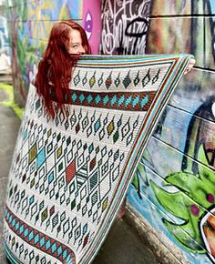 a woman with red hair is holding up a blanket in front of graffiti covered walls