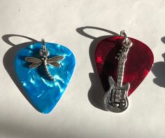 three guitar picks with dragonfly pendants on them sitting next to each other in the shape of guitars