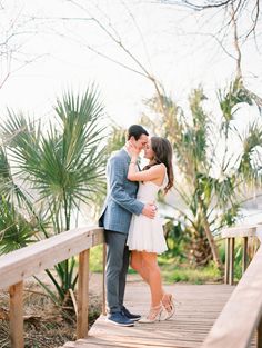 a bride and groom kissing on a wooden bridge in front of palm trees at their wedding