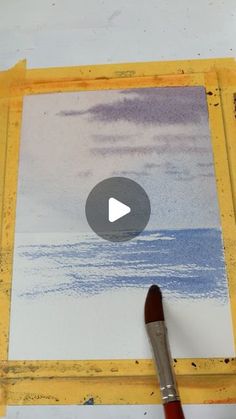 a paintbrush is sitting on top of a piece of paper that has been painted with watercolors