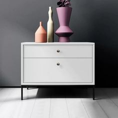 two vases are sitting on top of a white chest of drawers in front of a gray wall