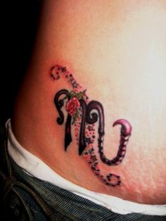 a woman's lower back tattoo with the letter u on it, and flowers