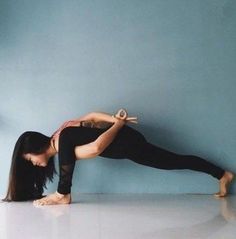 a woman is doing yoga on the floor in front of a blue wall with her legs spread out