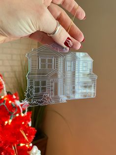 a person holding up a cutout of a house in front of a christmas tree