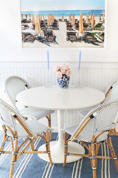 a white table with four chairs and a vase filled with flowers on top of it