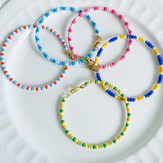 four bracelets are sitting on a white plate with a gold chain and colorful beads