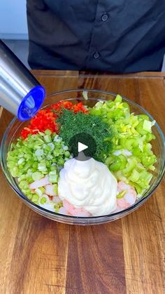 a bowl filled with vegetables and dressing on top of a wooden table next to a blender