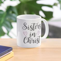 a white coffee mug with the words sisters in christ printed on it next to some books