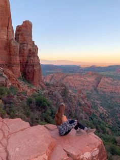 a woman sitting on top of a large rock next to a valley filled with trees