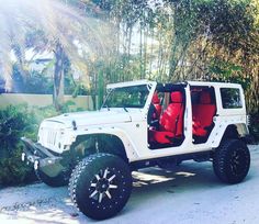 a white jeep with red seats is parked in front of some trees and palm trees