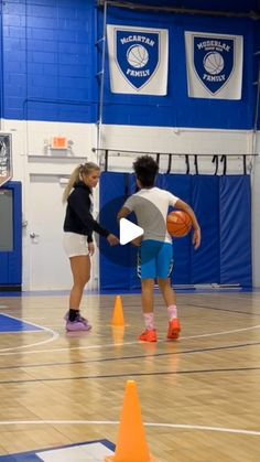 two girls are playing basketball in an indoor gym with cones on the floor and blue walls