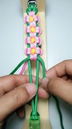 two hands are working on a piece of string with pink and yellow flowers attached to it