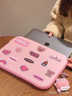 a woman sitting at a table with a pink laptop covered in stickers on it