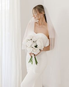 a woman in a white wedding gown holding a bouquet of flowers and wearing a veil