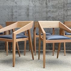 four wooden chairs sitting next to each other in front of a concrete wall and cement floor