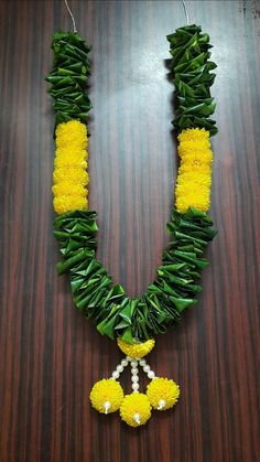 a necklace made out of yellow flowers and green leaves on a wooden table with beads hanging from it