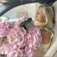 a woman sitting in the back seat of a car holding a bouquet of pink flowers