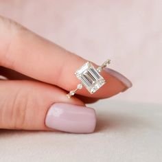 a woman's hand holding an engagement ring with a diamond in the middle and two diamonds on each side