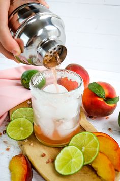 someone is pouring something into a glass with ice and fruit on the table next to it