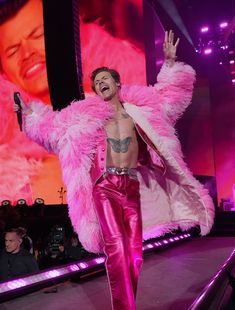 the man is dressed in pink and has his arms out as he walks on stage