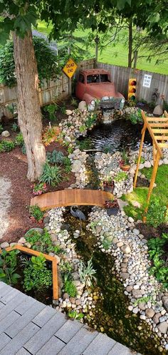 a car is parked in the back yard next to a small pond and bridge with rocks on it