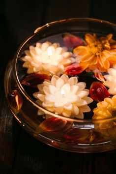 flowers floating in water on top of a glass bowl filled with water and lit candles