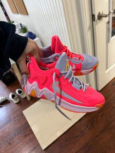 someone is holding up a pair of pink and grey sneakers on the floor in front of a door