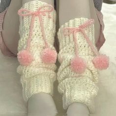 a pair of white crocheted slippers with pink pom - poms