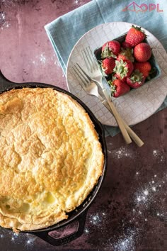 a close up of a pie in a pan on a table with strawberries next to it