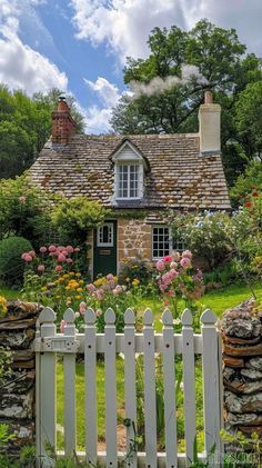 a white picket fence in front of a stone house with flowers and trees around it