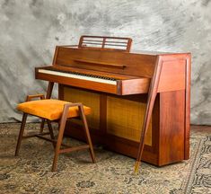 an old piano sitting on top of a rug next to a chair and ottoman in front of a wall