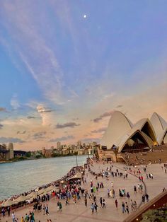 many people are walking around in front of the sydney opera house at sunset or dawn