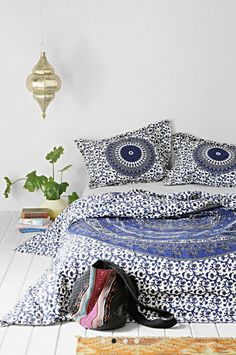 a bed with blue and white designs on the sheets, pillows and rugs next to a plant