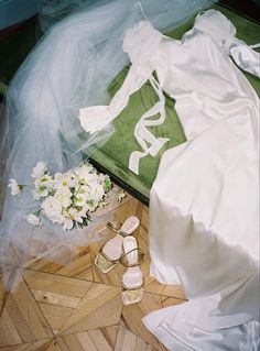 a wedding dress and shoes on the floor next to a bouquet of white flowers in a vase