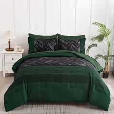 a bed with green comforters and pillows in a white room next to a potted plant