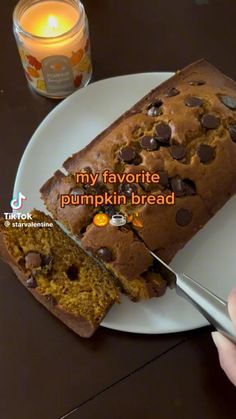 someone is cutting into a pumpkin bread on a plate with a candle in the background