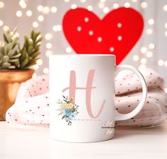 a white coffee mug sitting on top of a table next to a potted plant