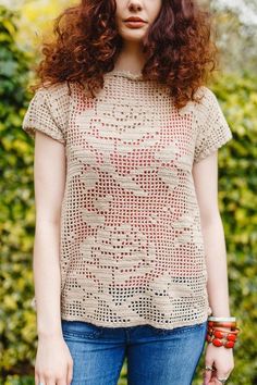 a woman with red hair is standing in front of some bushes and holding a handbag